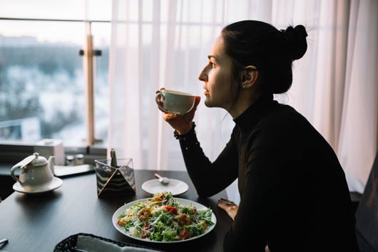 Persona tomando una bebida junto a una ensalada como parte de una alimentación saludable