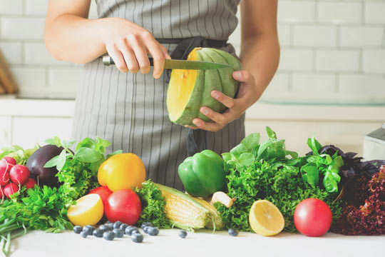 Persona pelando calabazas, verduras, cebolla, tomates, maíz, pimiento, espinacas, hojas de lechuga.