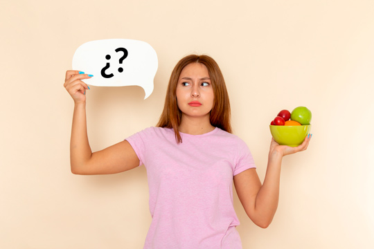 Vista frontal mujer con plato lleno de frutas y letrero con interrogantes frutas alimentos vitamina