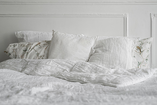 Cama con ropa blanca y almohadas confortables preparada para garantizar un descanso reparador y una buena higiene del sueño.