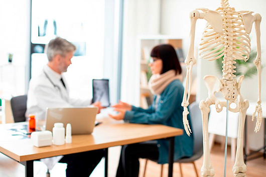Esqueleto en la sala de examen del hospital con personas en segundo plano