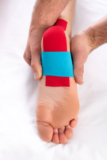 Persona aplicando cintas de kinesiología en el pie de una persona en el sofá de masaje