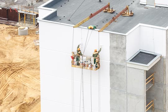 Dos personas trabajadoras en una grúa pintan la pared de un edificio residencial de gran altura