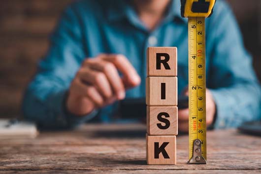 Bloques de madera formando la palabra RISK junto a una cinta métrica, representando la medición de riesgos