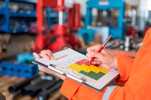 Trabajador industrial con uniforme naranja completando una matriz de evaluación de riesgos en un portapapeles dentro de un taller mecánico.