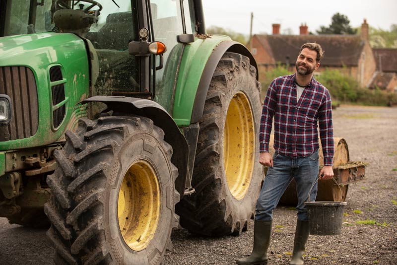 Trabajador agrario sonriendo junto a un tractor.